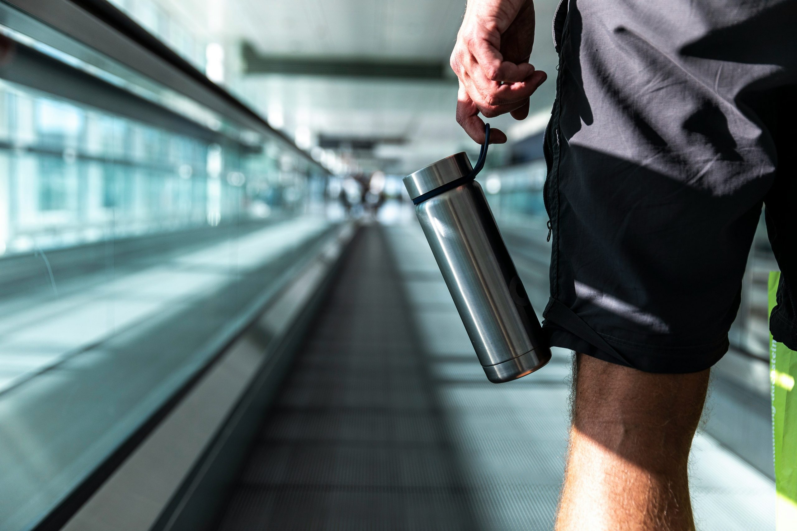 man on indoor travelator holding silver bottle