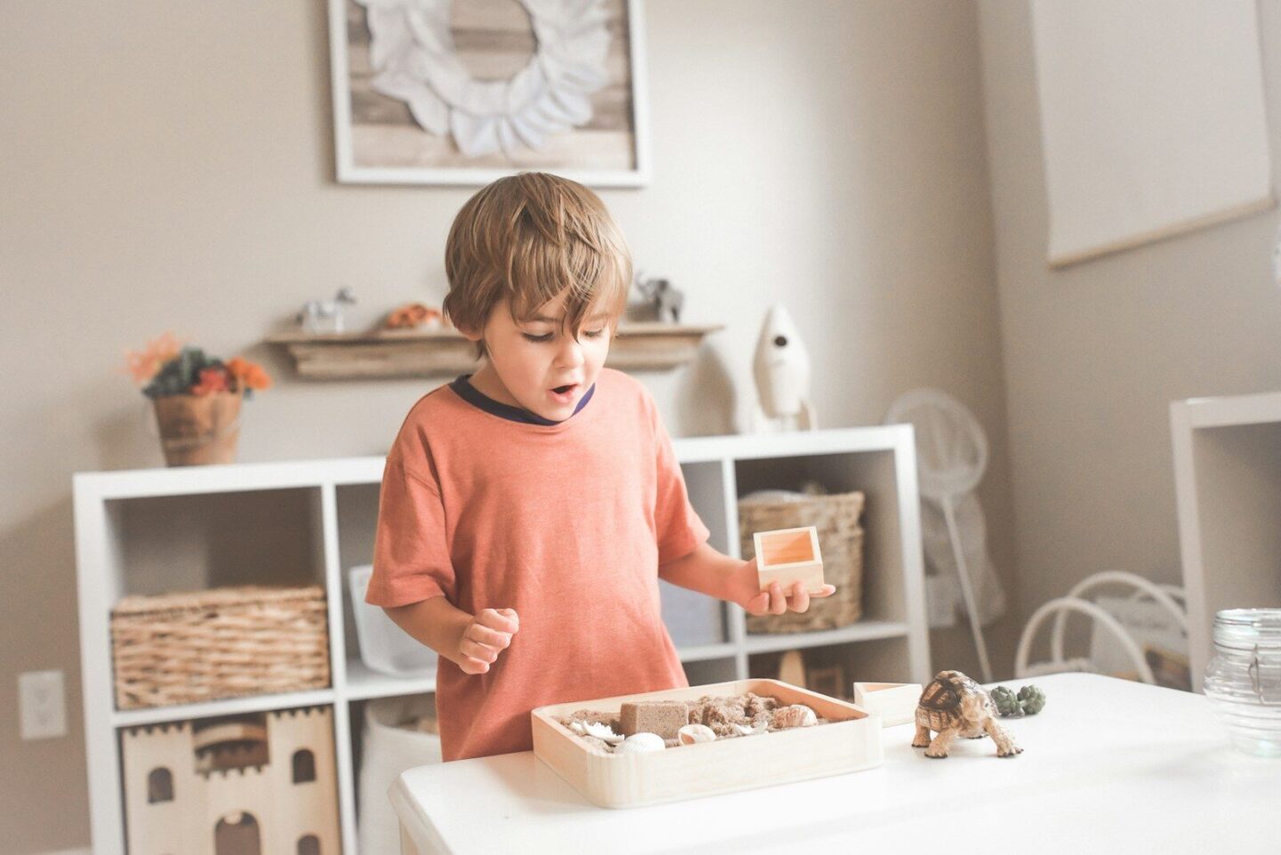 boy in orange t-shirt standing in front of white wooden table with toys on it
