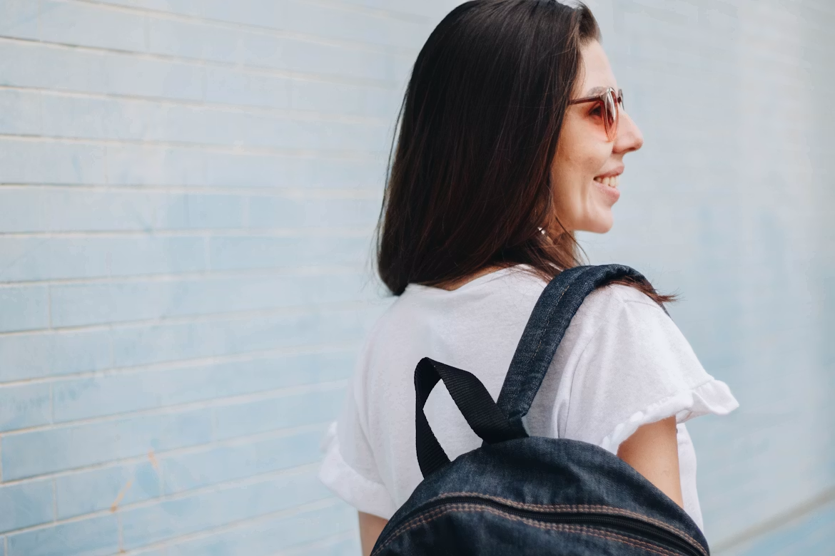 woman wearing white t-shirt and backpack, turning her head and smiling