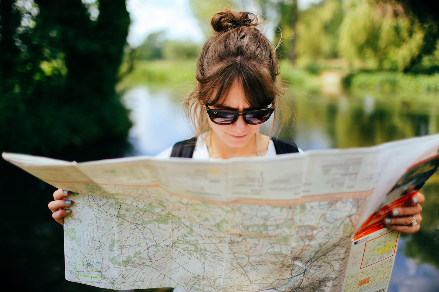 woman with dark brown hair and wearing sunglasses standing outside holding an open map