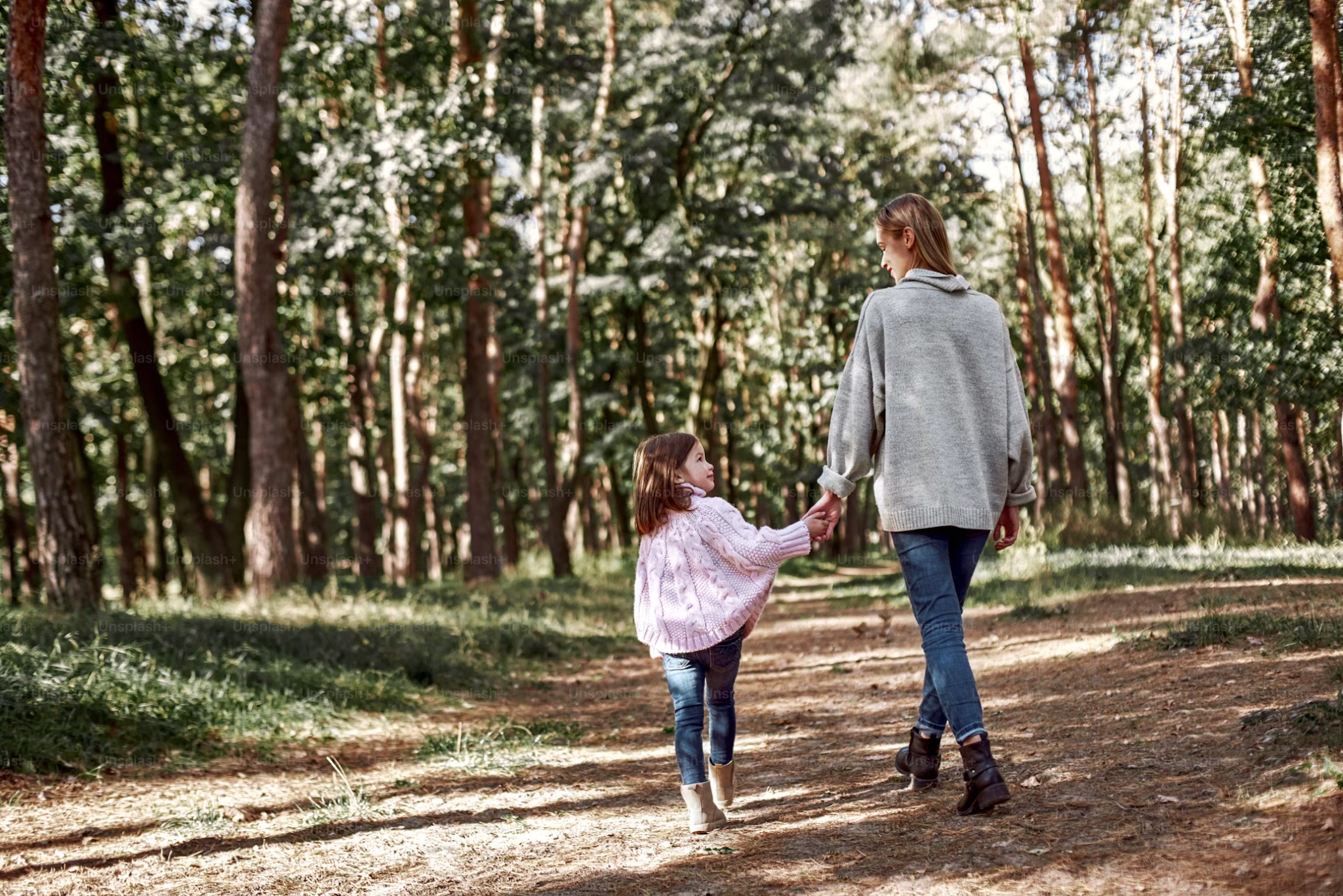 woman and child holding hands and walking through forest