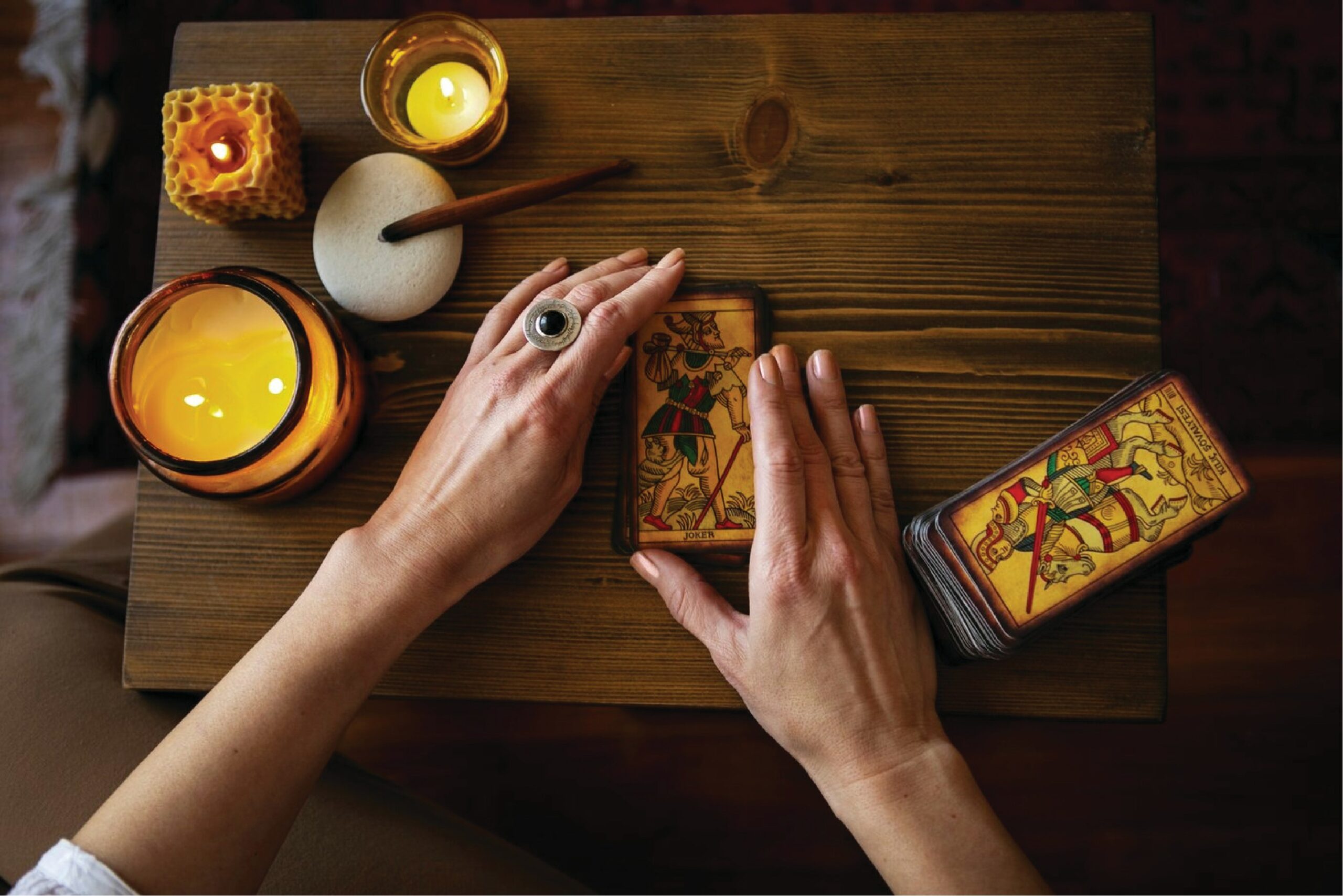 a woman's hands holding tarot cards on wooden table next to candles
