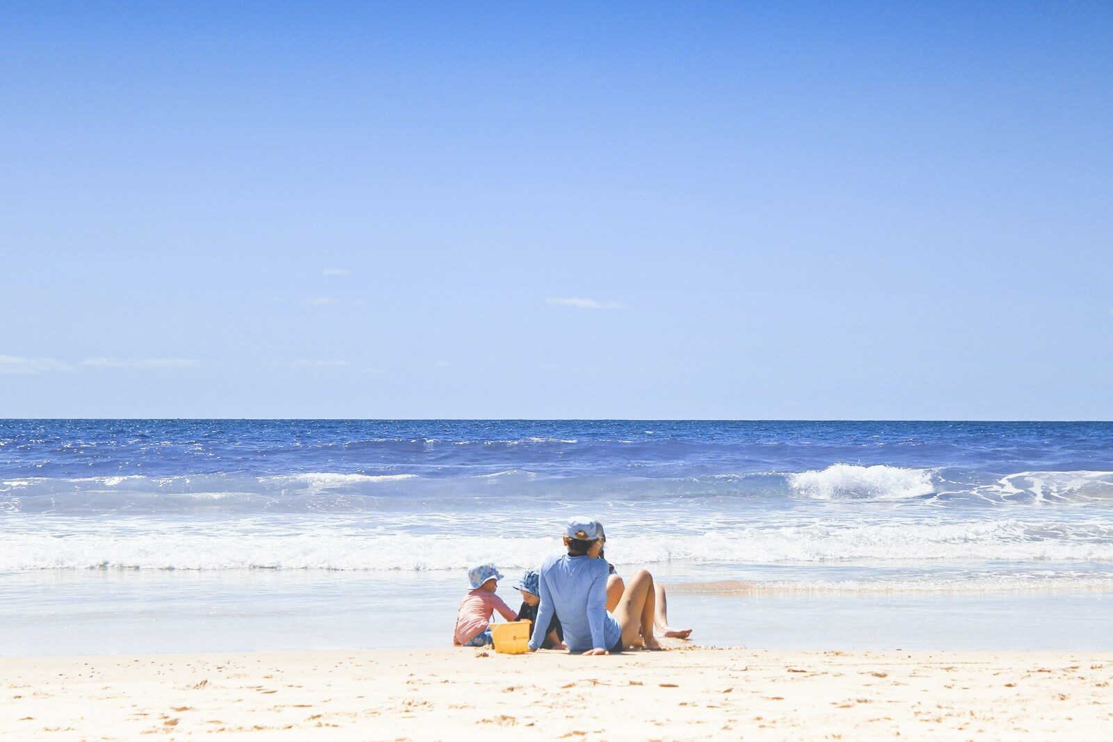 family sitting on beach with blue sea and sky
