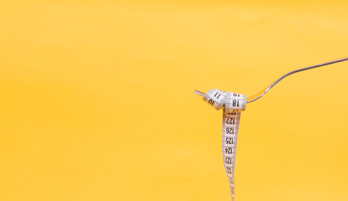 tape measure wrapped around fork, in front of a bright yellow background