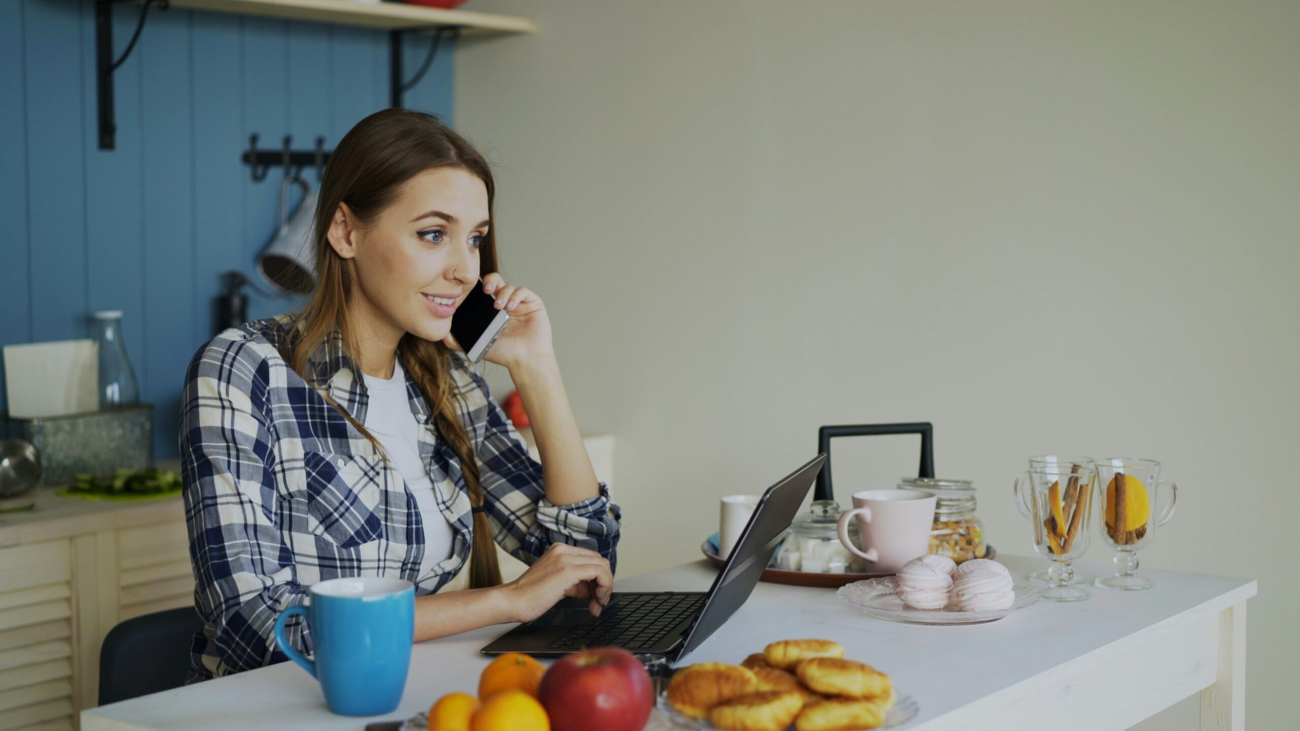 A woman working on a laptop at a kitchen table beside a coffee cup