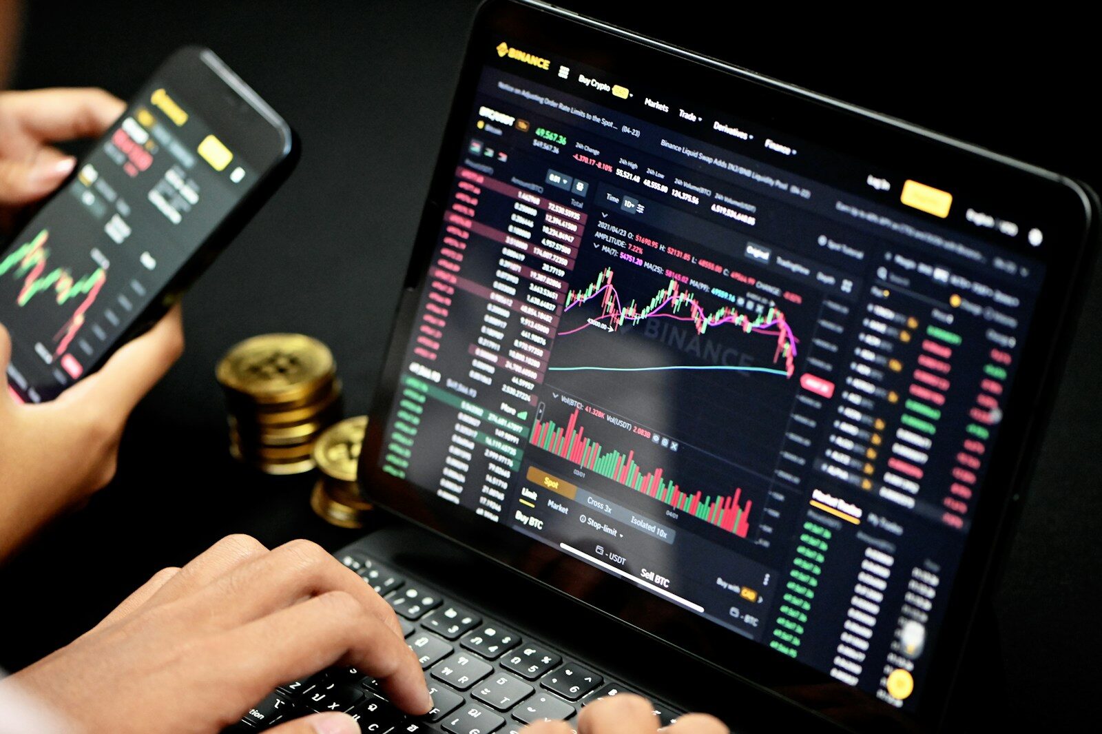 person using black laptop computer with charts and figures on screen, with persons hands holding phone next to them
